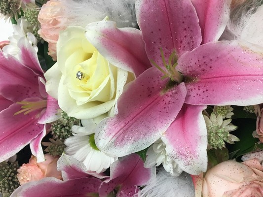 Heart-shaped funeral tribute in pink and white with luxury flowers, white feathers, glitter, and diamantes.