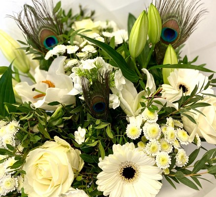 White seasonal florist’s choice hatbox arrangement with greenery and peacock feathers.