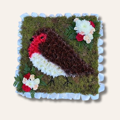 Red robin-shaped funeral tribute on a 2ft x 2ft moss base, created with chrysanthemum flowers, pipe cleaner detailing and ribbon edging.