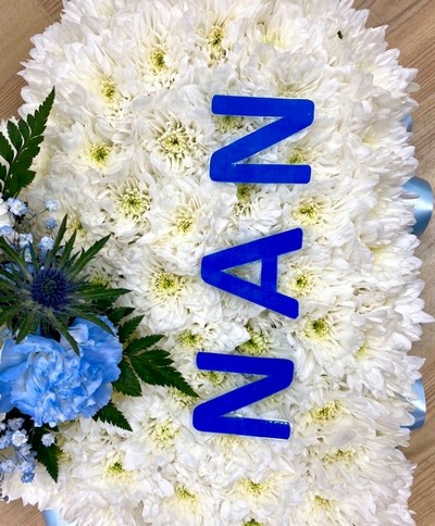 Heart-shaped funeral tribute with laminated wording, white chrysanthemums, delicate ribbon edge, and matching focal. Customisable colour options available.