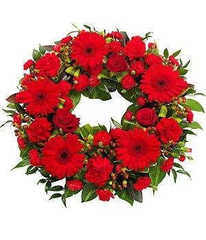 Red funeral wreath with mixed seasonal flowers and lush green foliage.
