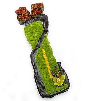 Golf bag-shaped funeral tribute made with Kermit chrysanthemum, featuring accent florals, pipe cleaner golf club detailing, and black leaf strap and handle, measuring approximately 90cm x 30cm.. 