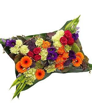 Brightly coloured pillow funeral tribute with luxury flowers in bold tones and textured foliage.