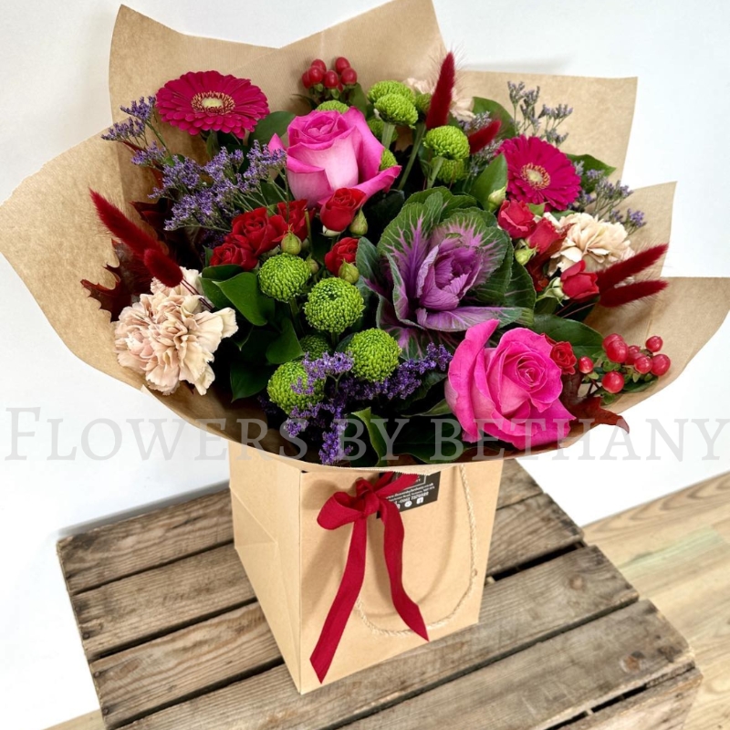 Autumn Jewel bouquet with fuchsia roses, gerbera, green chrysanthemums, berries and ornamental cabbage in kraft wrap.