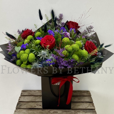 Elena bouquet with red roses, lime green blooms, purple flowers and thistle blue, hand-tied in black wrap.