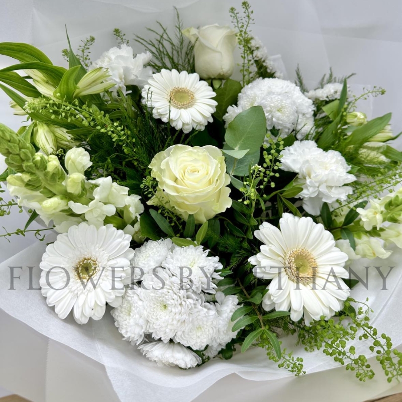 White and green hand-tied bouquet with mixed seasonal florals and foliage, presented in a white gift bag.