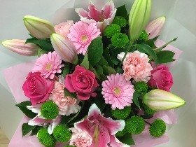 Hand-tied bouquet of pink lilies, pink roses, pink germini and lime chrysanthemums with mixed foliage in a gift bag.