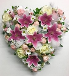 Heart-shaped funeral tribute in pink and white with luxury flowers, white feathers, glitter, and diamantes.