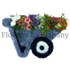 Wheelbarrow-shaped funeral tribute filled with vibrant seasonal flowers, with the option to include fresh fruit and vegetables, measuring approximately 91cm x 57cm.