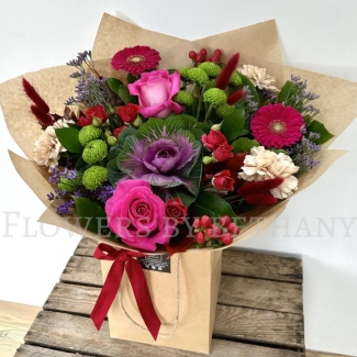 Autumn Jewel bouquet with fuchsia roses, gerbera, green chrysanthemums, berries and ornamental cabbage in kraft wrap.