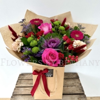 Autumn Jewel bouquet with fuchsia roses, gerbera, green chrysanthemums, berries and ornamental cabbage in kraft wrap.