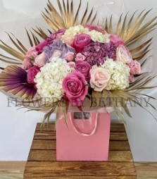 Luxury bouquet of roses, spray roses and hydrangea with gold leaf and ombré palm, presented in a pink gift bag.