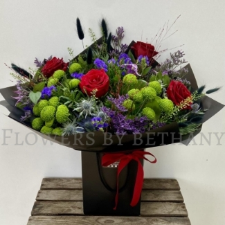 Elena bouquet with red roses, lime green blooms, purple flowers and thistle blue, hand-tied in black wrap.