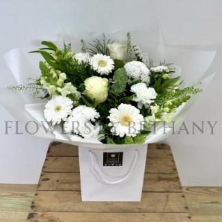 White and green hand-tied bouquet with mixed seasonal florals and foliage, presented in a white gift bag.